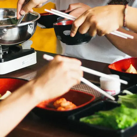 Hands reaching across a shared table set with a hot pot and side dishes