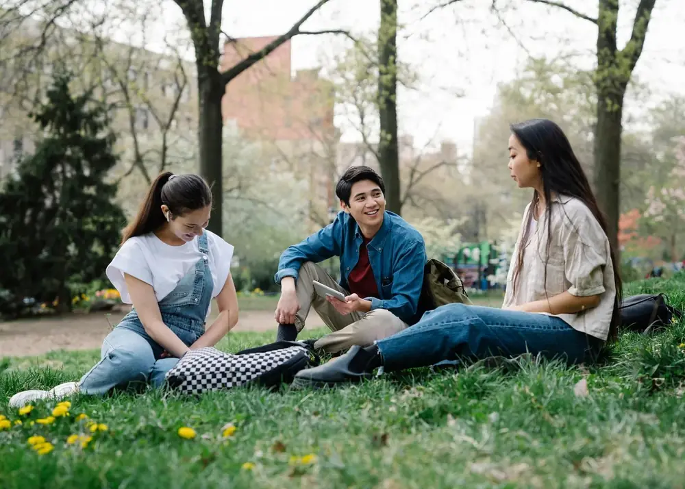 Three young adults sitting together on grass in a park, mid-conversation
