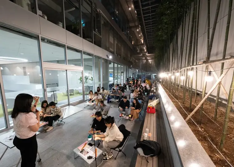 People seated at low tables along a lantern-lit outdoor walkway at night, bamboo screening one side